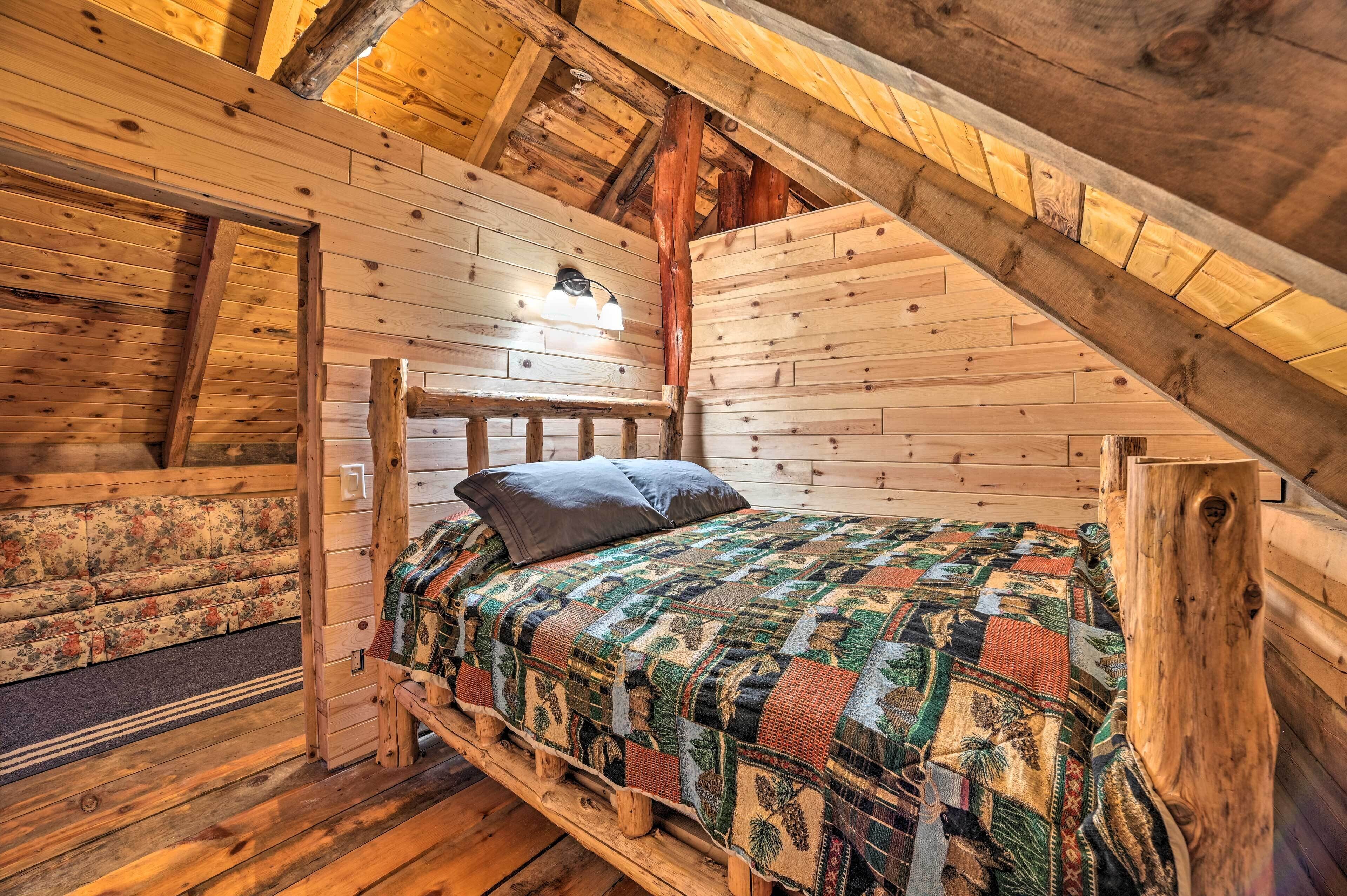 Une cabane en bois avec une chambre à coucher située en mezzanine, comprenant un lit en bois, une couvre-lit matelassée et une table de chevet.