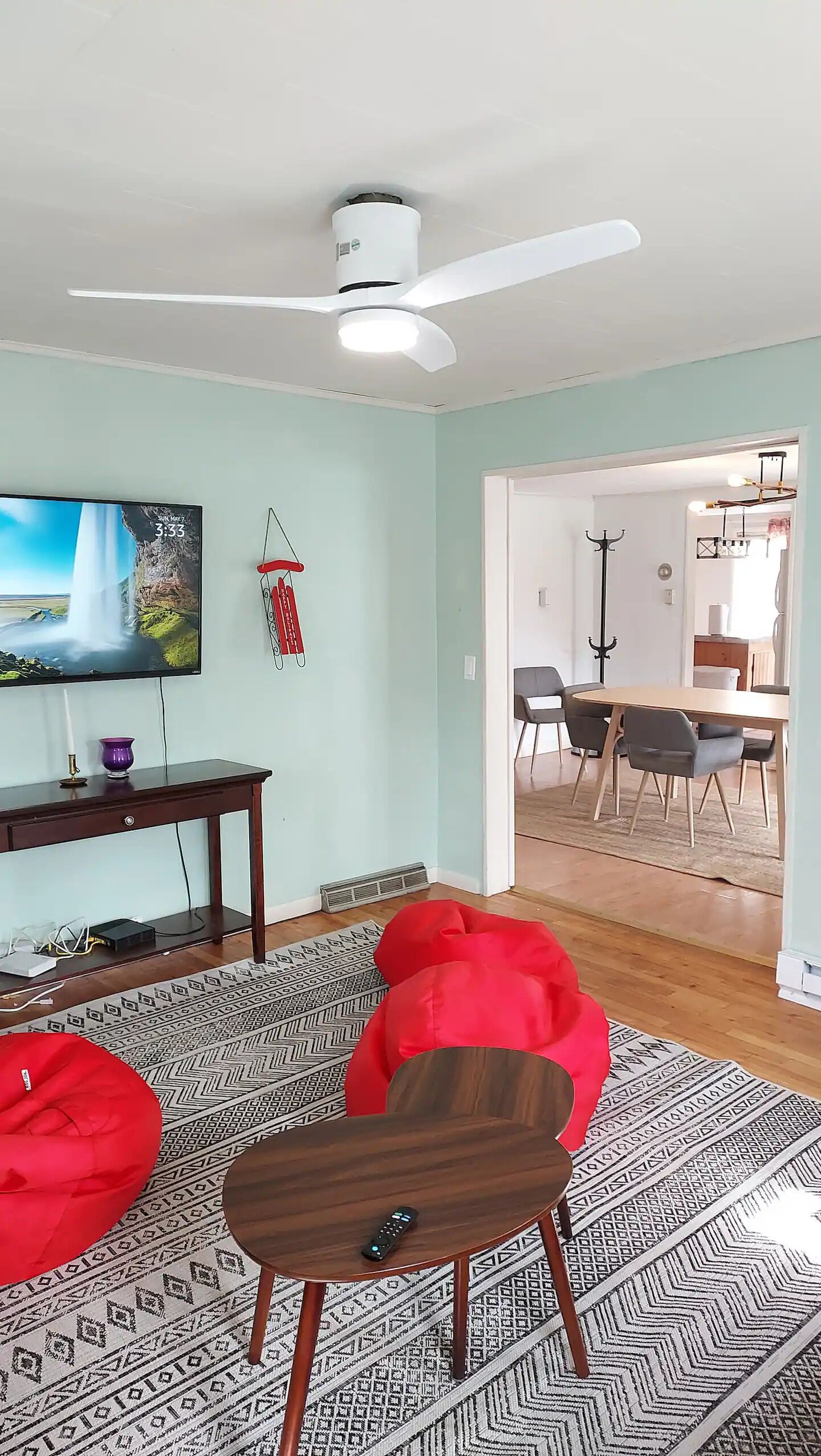 Un salon équipé d’un téléviseur à écran plat, d’un ventilateur de plafond, d’un coin repas avec des chaises et d’un tapis à motifs.