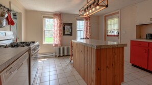 A kitchen with a central island, white tiled floor, wooden cabinets, and a red fridge.