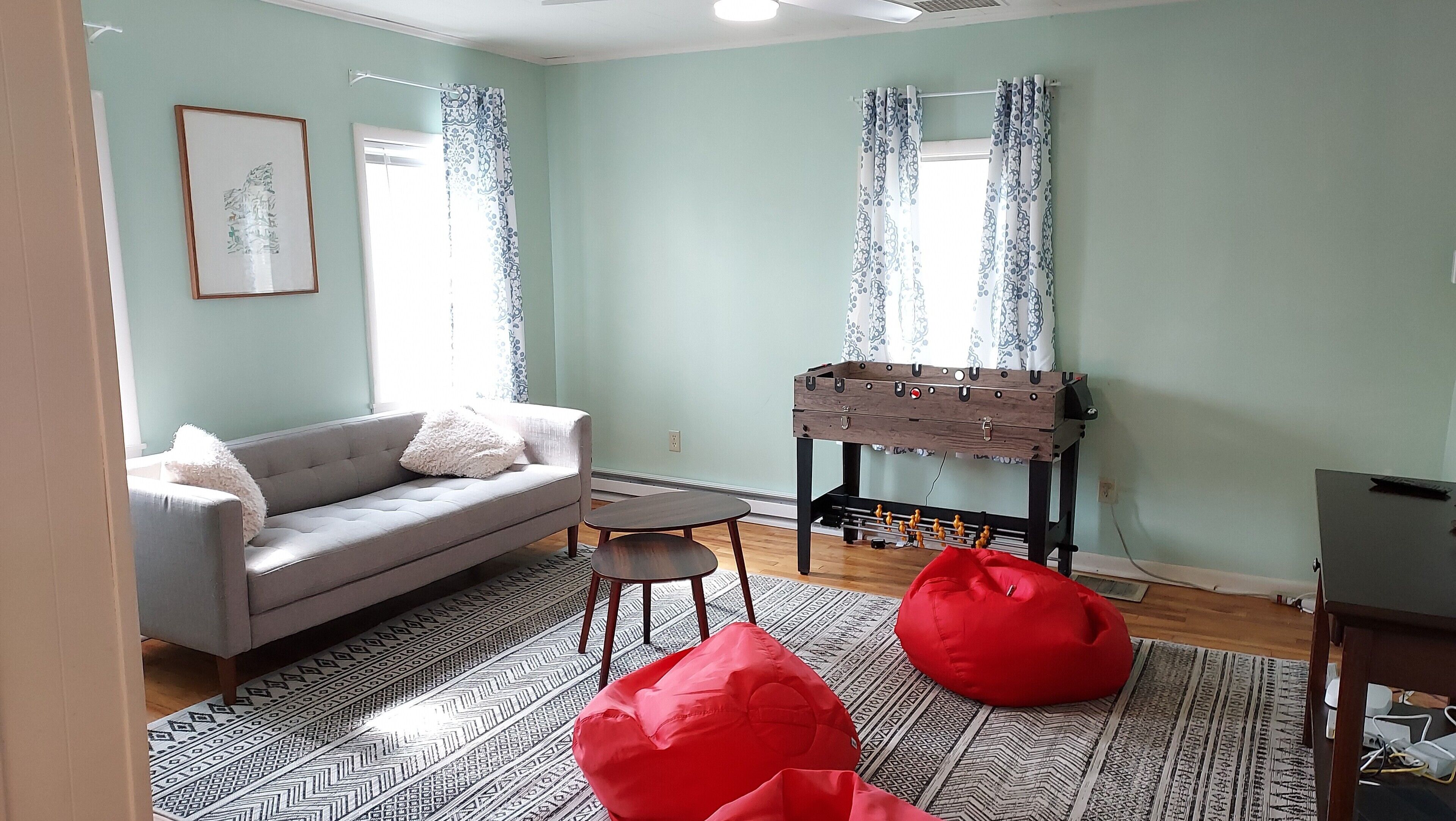 A living room with a sofa, a small table, a red bean bag, a wooden side table, and a foosball table.