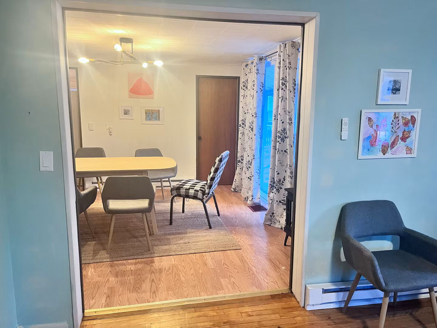 Een interieur met een houten vloer, een eettafel met stoelen, een blauwe fauteuil en een deur naar een andere kamer.