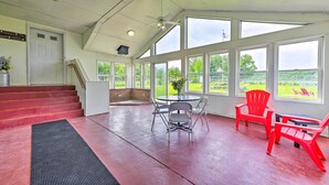 A spacious room with a large window, a table with chairs, a red chair, and a staircase. - Stunning Wisconsin Retreat on Active Farm! (Arena)