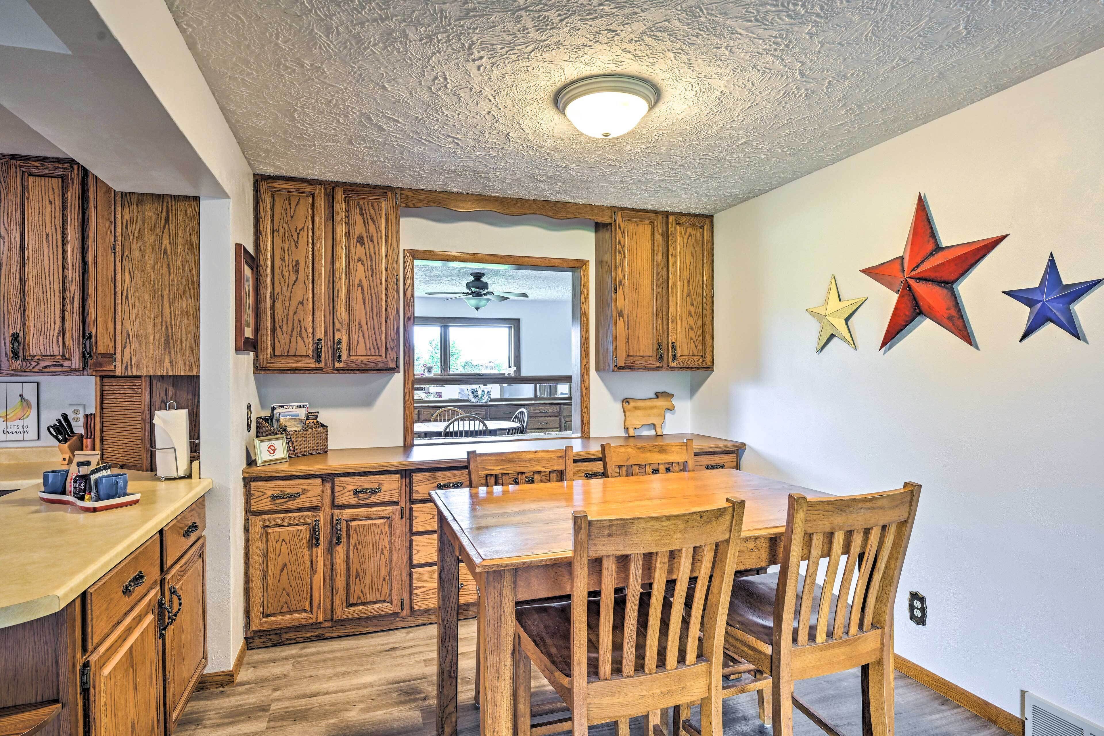 A kitchen with wooden cabinets, a dining table, and chairs. There is a ceiling fan and a window.