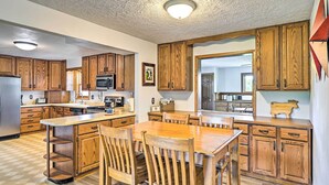 A kitchen with wooden cabinets, a central island with chairs, and a microwave. - Stunning Wisconsin Retreat on Active Farm! (Arena)