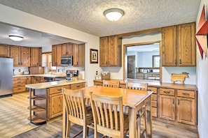 Una cocina con armarios de madera, una isla central con sillas y un microondas.