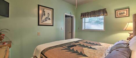 A bedroom with a bed, a ceiling fan, a window with blinds, and framed pictures on the wall.