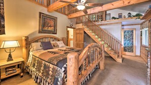 A bedroom with a wooden bed, a nightstand, a ceiling fan, a staircase, and a window with a view of the outdoors. - Tenn River Cabin w/ Hot Tub - 10 Mi to Chattanooga (Chattanooga)