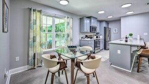 A modern kitchen with grey cabinets, a central island, and a dining area with a glass table and chairs.