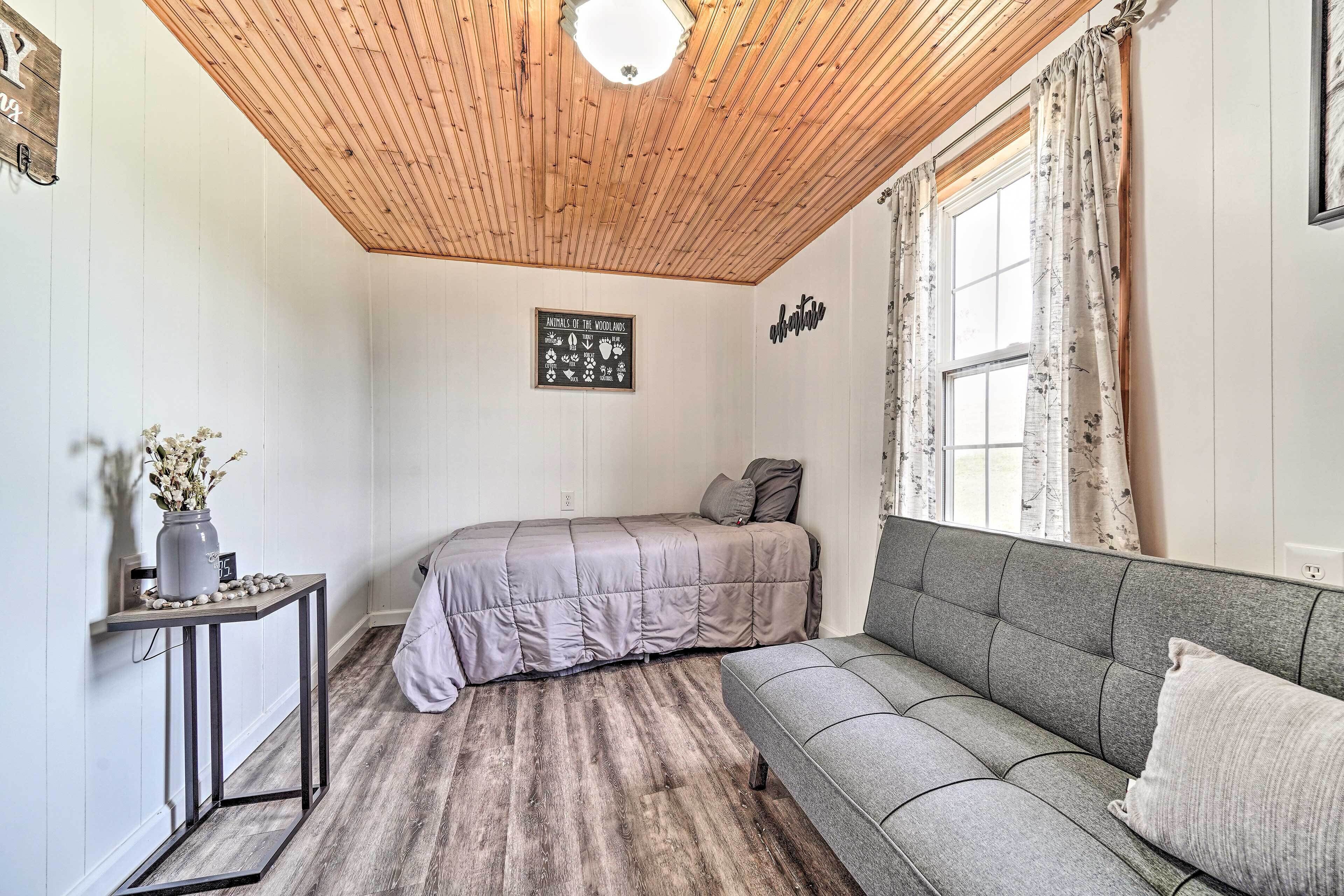 A room with a wooden ceiling, a bed, a sofa, a small table with a vase, and a wall sign.