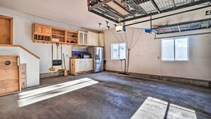 A spacious garage with a concrete floor, wooden cabinets, a refrigerator, and a ceiling with metal racks.
