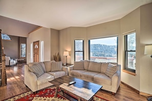 A spacious living room with a large window, a wooden coffee table, and a beige sofa with patterned cushions. - Spacious Evergreen Home w/ Hot Tub & Deck! (Evergreen)
