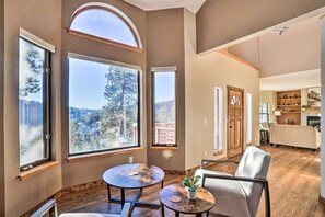 A spacious living area with large windows offering mountain views, a cozy seating arrangement, and a kitchen area visible in the background. - Spacious Evergreen Home w/ Hot Tub & Deck! (Evergreen)