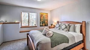 A bedroom with a wooden bed, a window with a view of trees, a painting on the wall, and a small shelf with a plant.