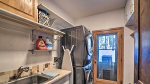 A compact kitchen with a stainless steel sink, a built-in washing machine, and a wooden door leading to a porch.