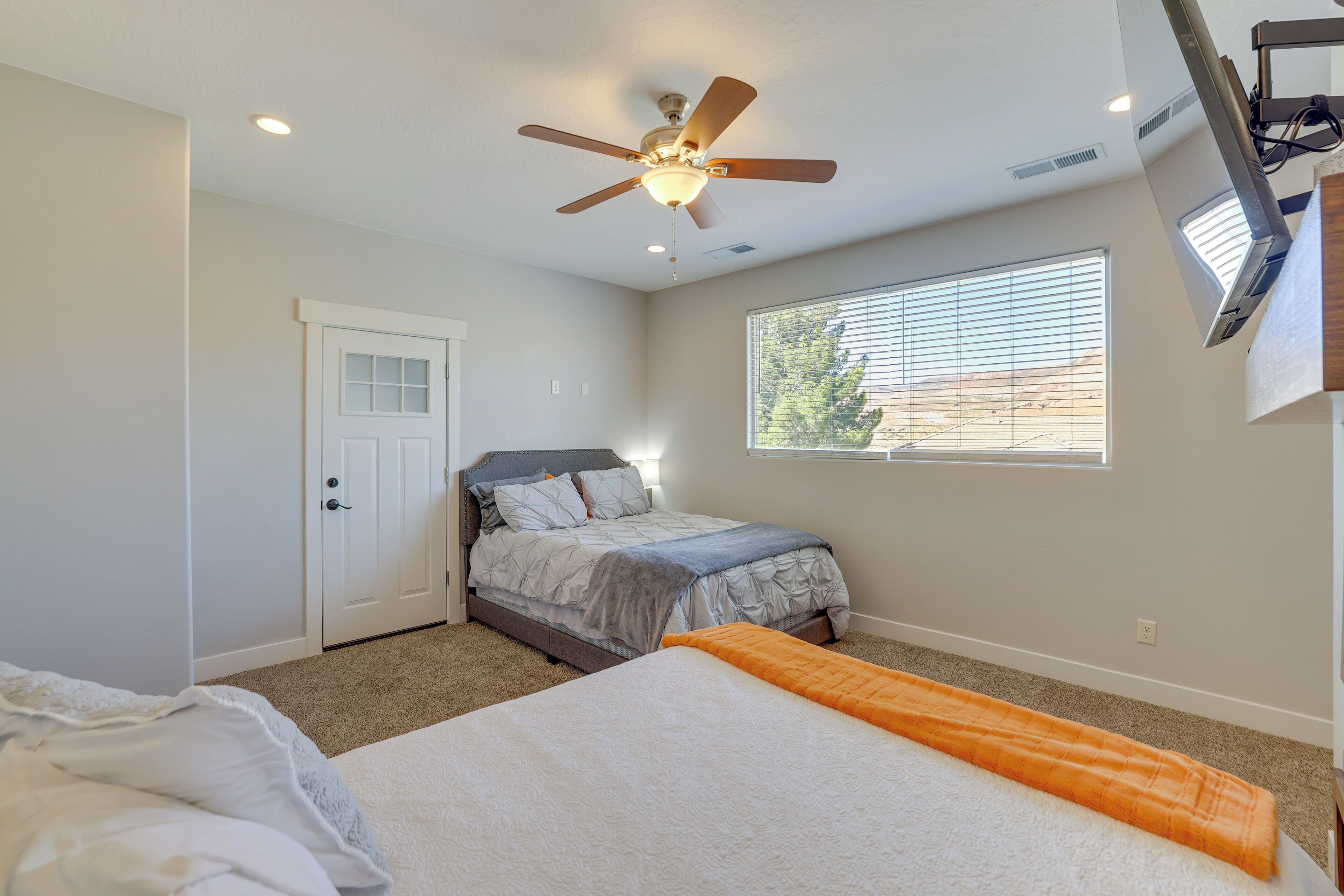 Un dormitorio con cama, ventilador de techo, ventana con persianas y puerta.