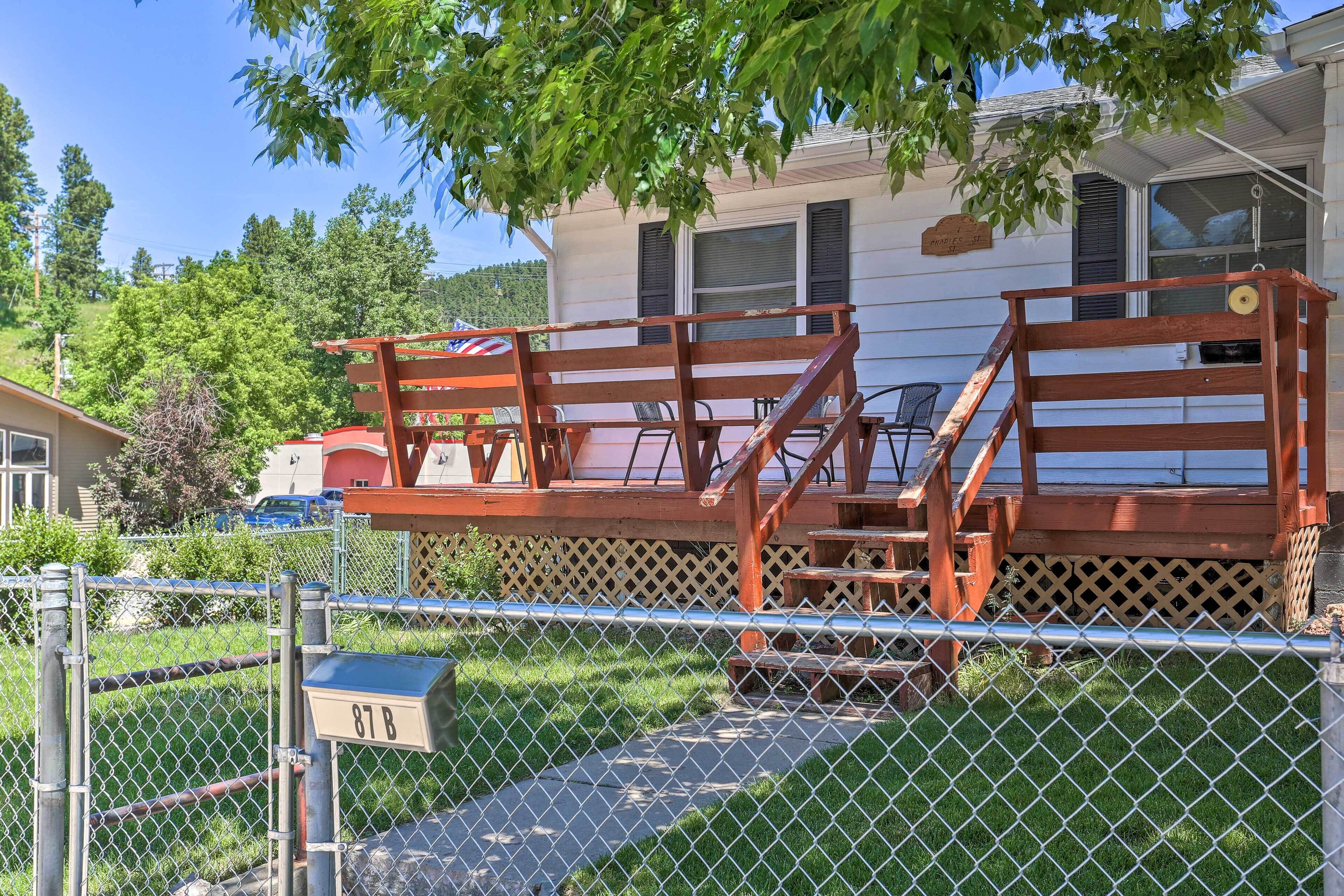Un espace extérieur clôturé, avec un banc en bois et une boîte aux lettres portant l’inscription « 87 B ».