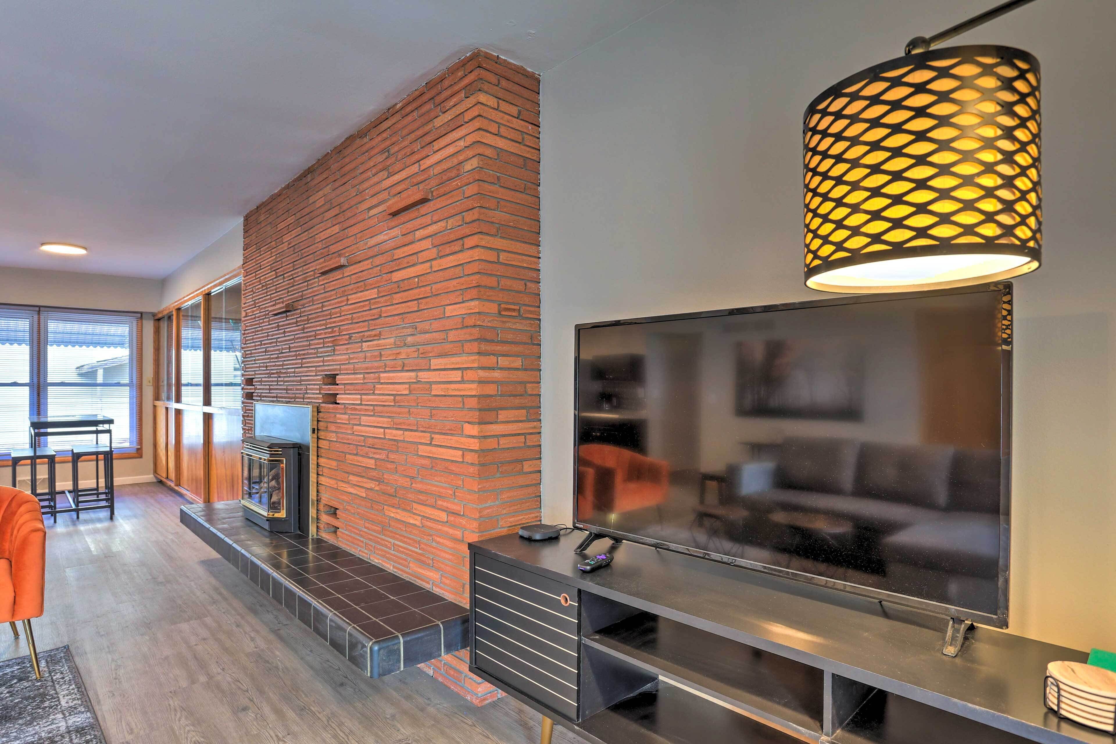 A modern living room with a brick fireplace, a flat-screen TV, and a stylish pendant light.