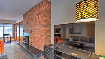 A modern living room with a brick fireplace, a flat-screen TV, and a stylish pendant light.