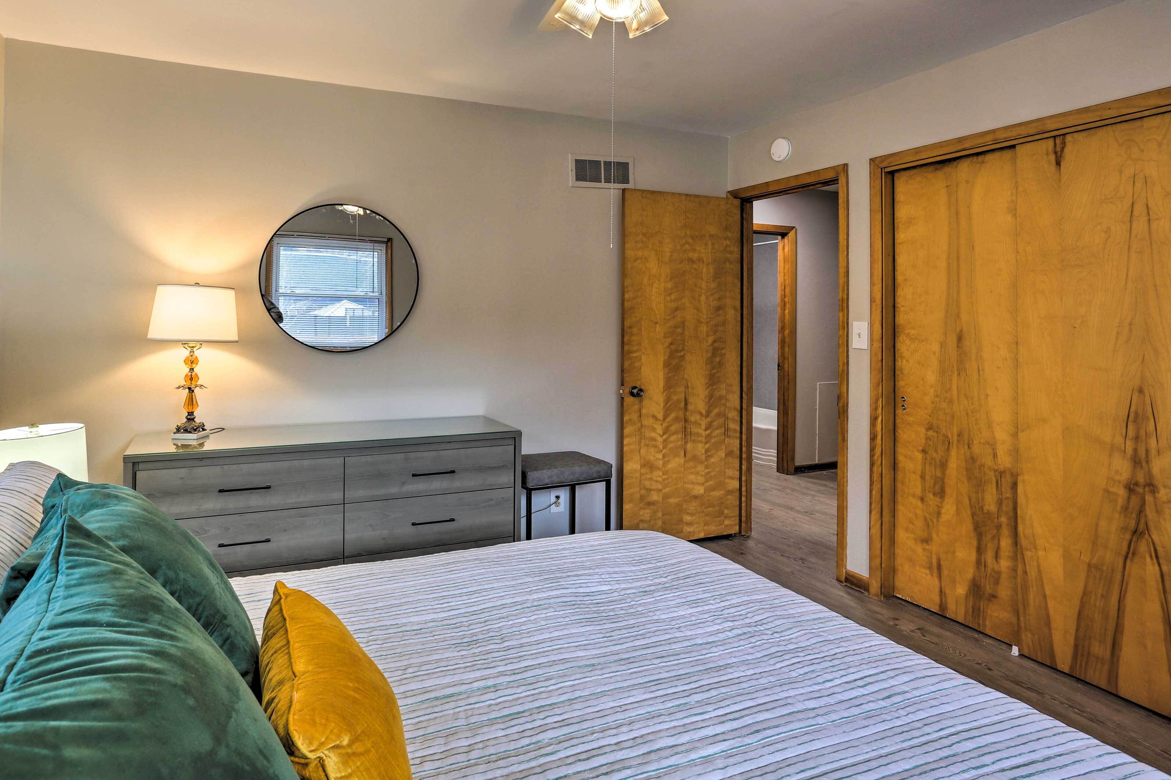 Ein Schlafzimmer mit Bett, Nachttisch mit Lampe, Kommode, Spiegel und Kleiderschrank.