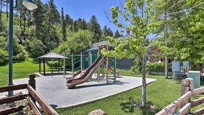 A playground with slides and a small shelter, surrounded by grass and trees.