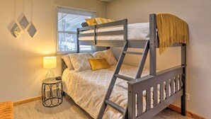 A bunk bed with a ladder, a bedside table with a lamp, and a window with blinds.
