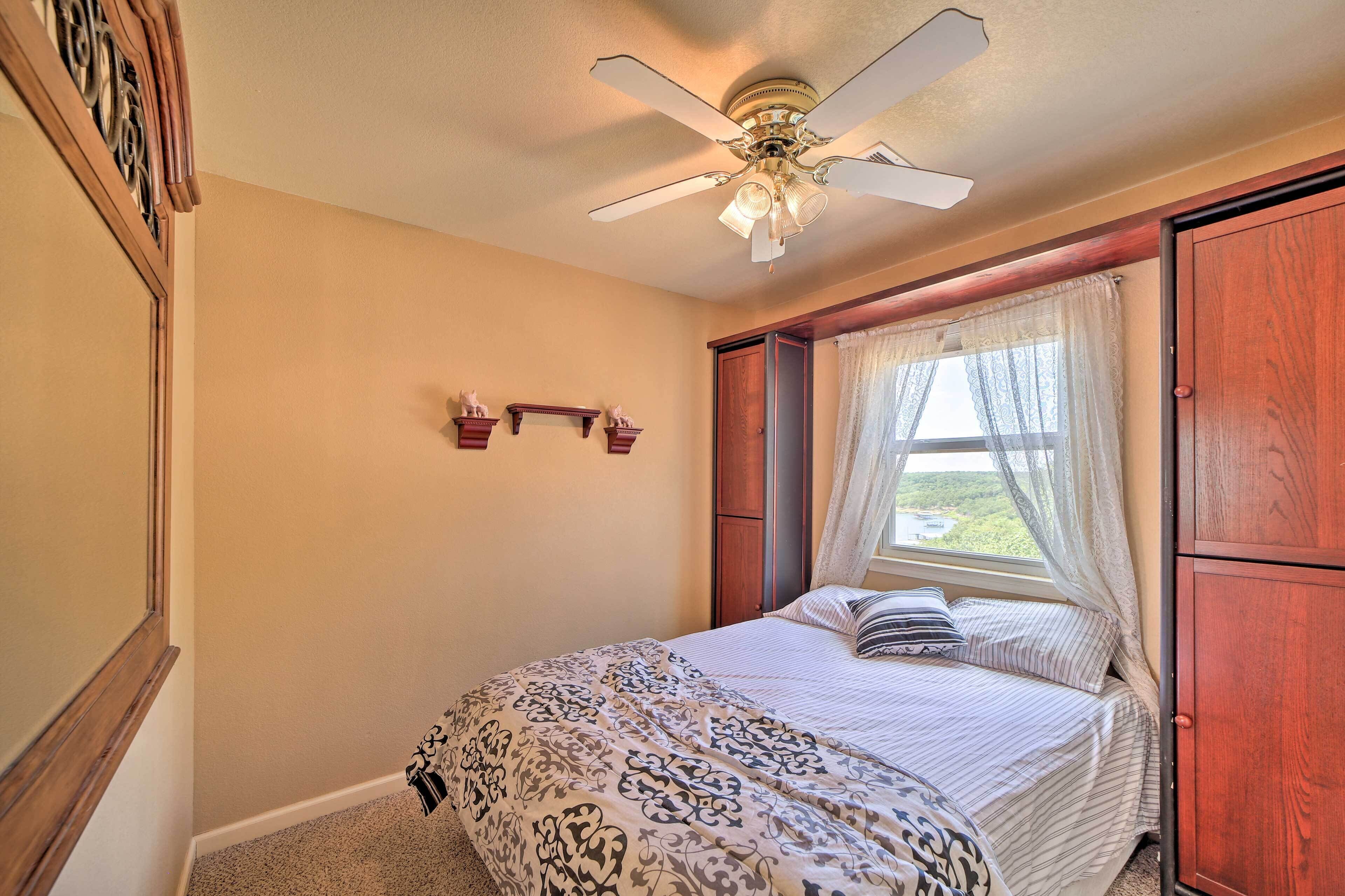 A bedroom with a bed, a ceiling fan, a window with curtains, and a wooden wardrobe.
