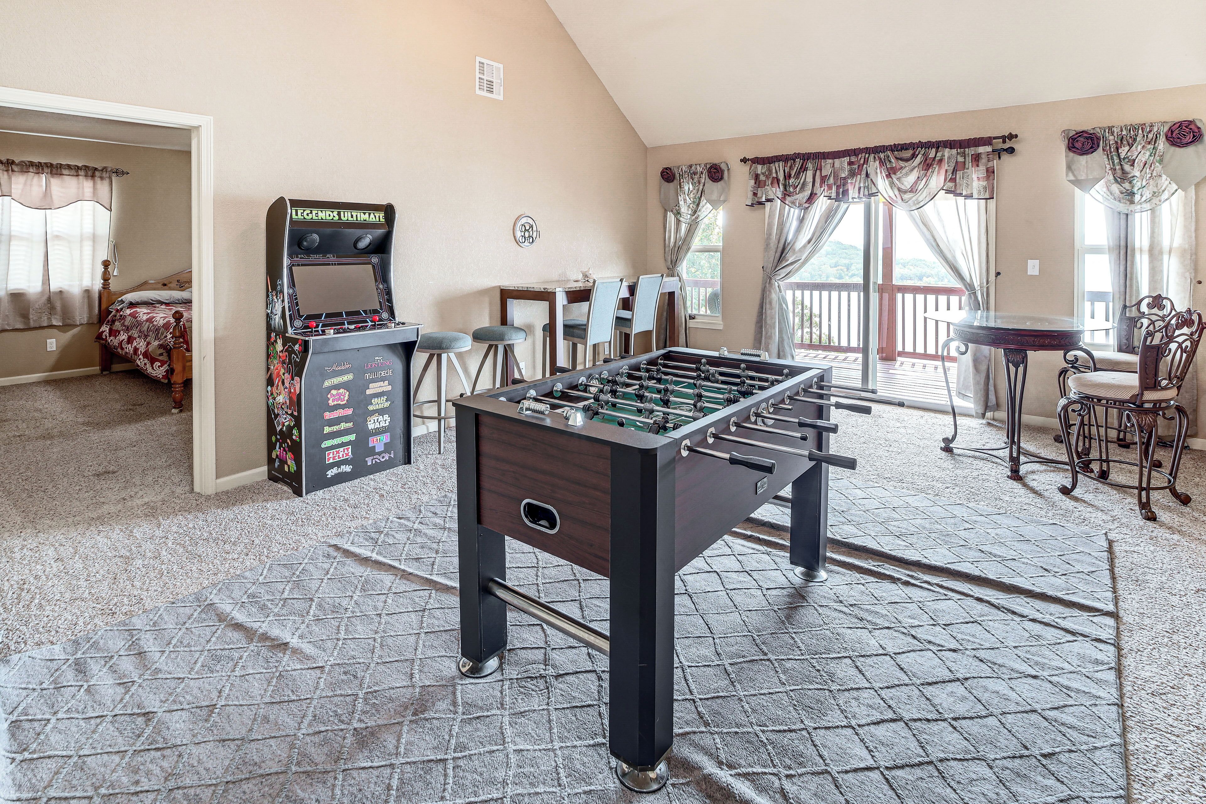 A room with a foosball table, a foosball machine, and a dining area with a table and chairs.