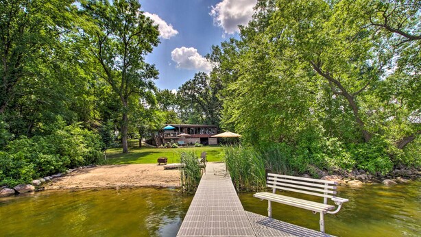 A wooden dock extending into a river, surrounded by lush greenery and a building with a blue roof in the background. - Year-round Waterfront Getaway: Lake Access + Dock! (South Haven)