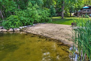 Una zona de arena junto a una masa de agua, rodeada de exuberante vegetación y árboles.