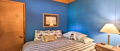 A bedroom with a wooden door, a bed with striped bedding, a framed picture on the wall, and a bedside lamp.