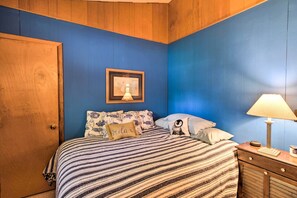 Une chambre avec une porte en bois, un lit avec une literie à rayures, un tableau encadré au mur et une lampe de chevet.
