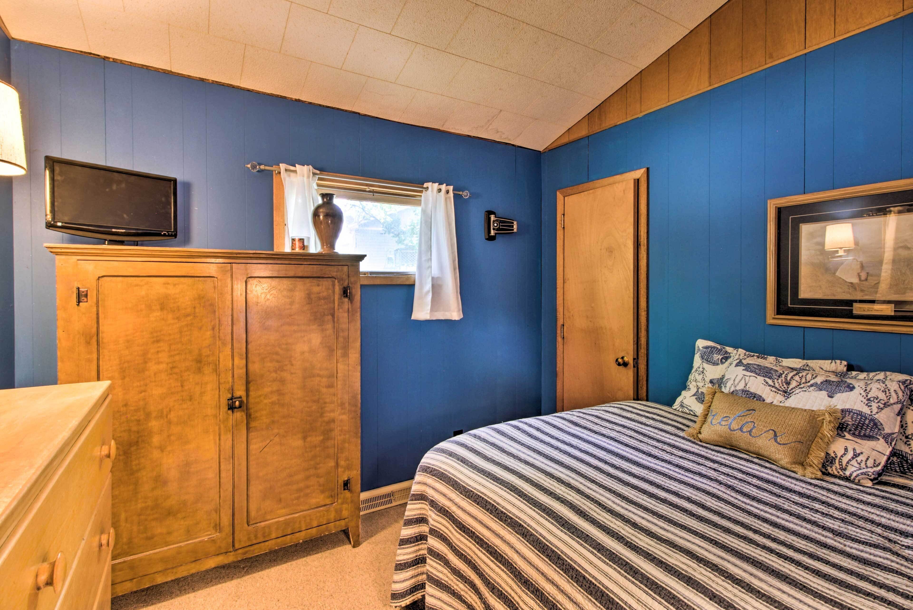 A bedroom with a bed, a wooden dresser, a television, and a window with curtains.