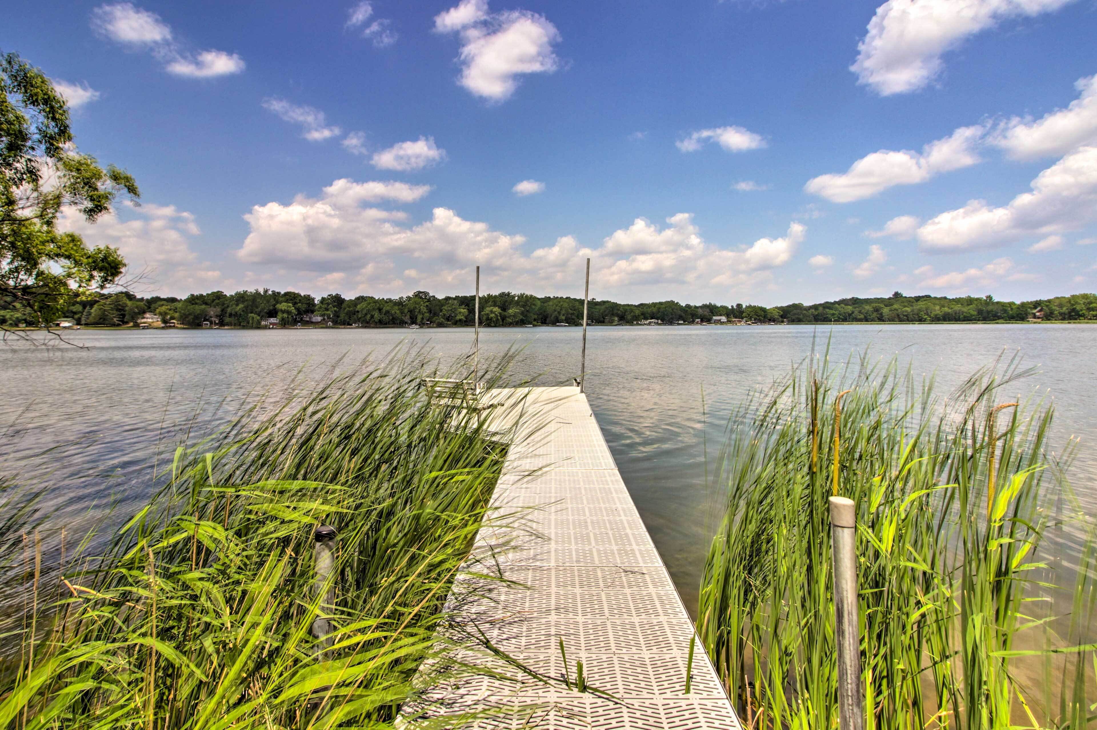 A wooden dock extending into a calm lake with surrounding greenery and a clear sky.