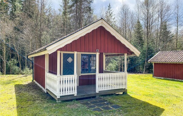 A small, single-story cabin with a porch and a covered entryway, surrounded by a forested area.