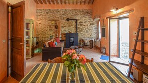 Ein gemütliches Zimmer mit Steinwand, Holzboden, Kamin, Sofa, Couchtisch und Blumenvase.