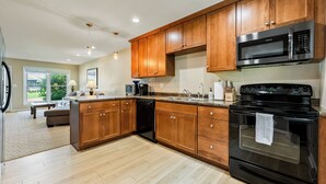 A modern kitchen with wooden cabinets, a black stove, and a built-in microwave. - Winona Lake Access With Pier (Warsaw)