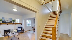 A spacious living room with a fireplace, a dining area, and a staircase with wooden railings. - Indiana Vacation Rental - Walk to Syracuse Lake! (Syracuse)