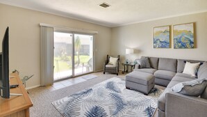 A living room with a grey sectional sofa, a coffee table, a flat-screen TV, and a large window with a view of the outdoors. - Florida Getaway - Balconies, Grill & Near Beaches! (Daytona Beach)