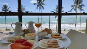 Ein Frühstückstisch mit verschiedenen Speisen und Blick auf das Meer und Palmen.