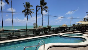 Ein Pool mit Meerblick, umgeben von Palmen und einer gefliesten Terrasse.