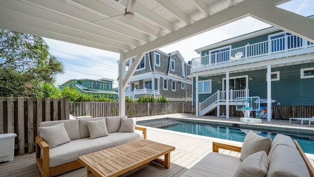 Un espace extérieur abrité comprenant une piscine, une terrasse en bois et une maison à deux étages dotée d’un balcon.