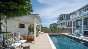 Un espace piscine doté d’un coin salon couvert, d’une terrasse en bois et d’une vue sur les maisons voisines.