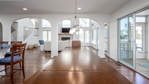Une cuisine spacieuse avec une longue table en bois, des murs blancs et de grandes fenêtres.