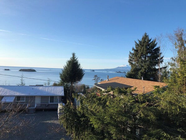 Zona residencial con una casa que tiene techo solar, rodeada de vegetación densa y vistas a una gran masa de agua con islas y una montaña distante.
