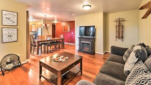 A living room with a wooden floor, a sofa, a dining table with chairs, a fireplace, and a television. - Near Skiing & Hiking: Inviting Retreat in Victor! (Victor)