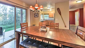 A dining area with a large wooden table, multiple chairs, and a bench. There is a chandelier with orange shades, a wooden paddle leaning against the wall, and a window providing a view of the outdoors. - Near Skiing & Hiking: Inviting Retreat in Victor! (Victor)