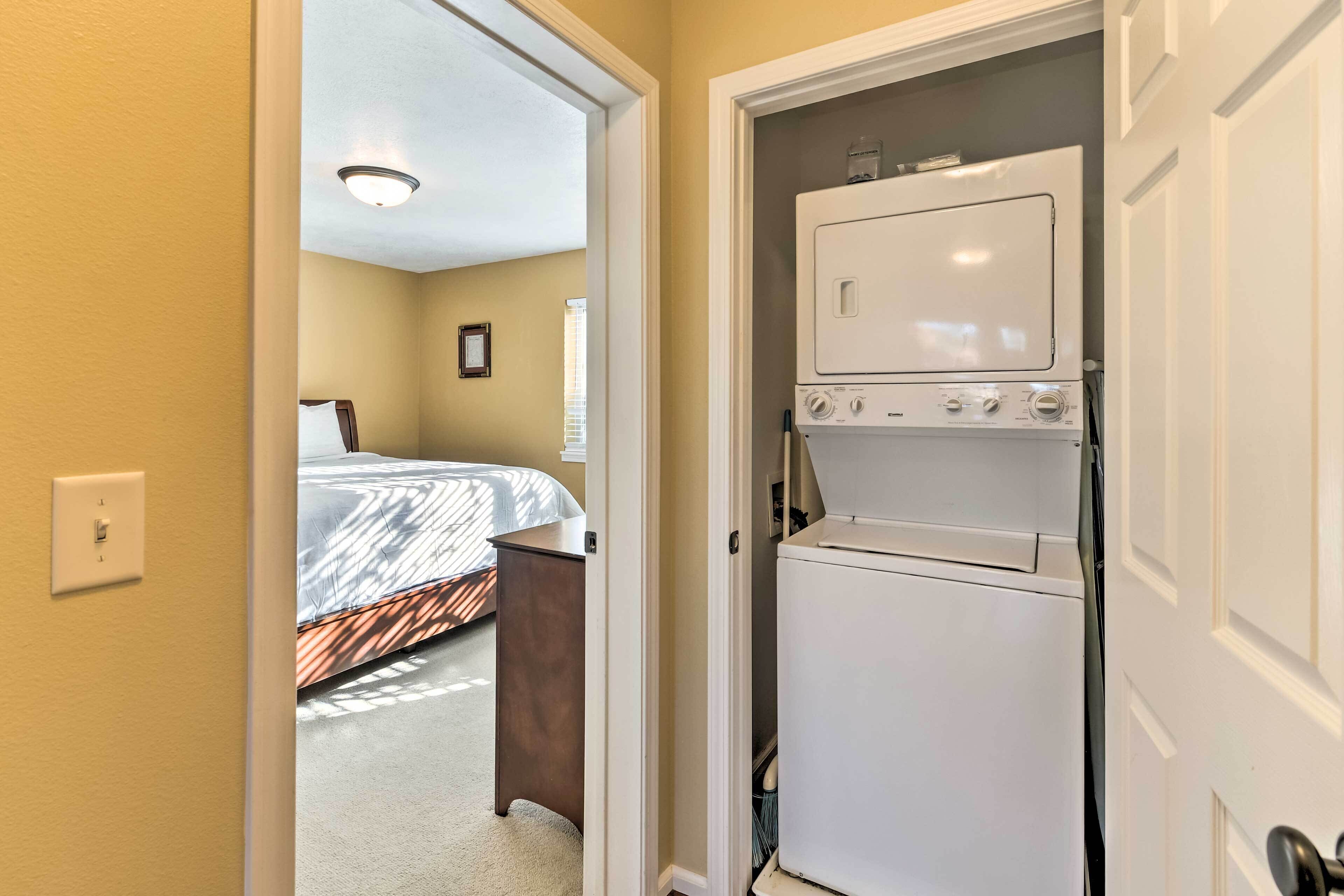 A compact hotel room with a bed, a small desk, and a white appliance, likely a washer and dryer, in a narrow hallway.