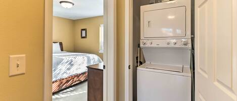 A compact hotel room with a bed, a small desk, and a white appliance, likely a washer and dryer, in a narrow hallway.