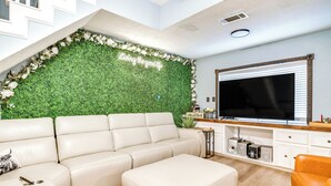 Een moderne woonkamer met een groene muur, een witte bank, een poef en een televisie op een houten dressoir.