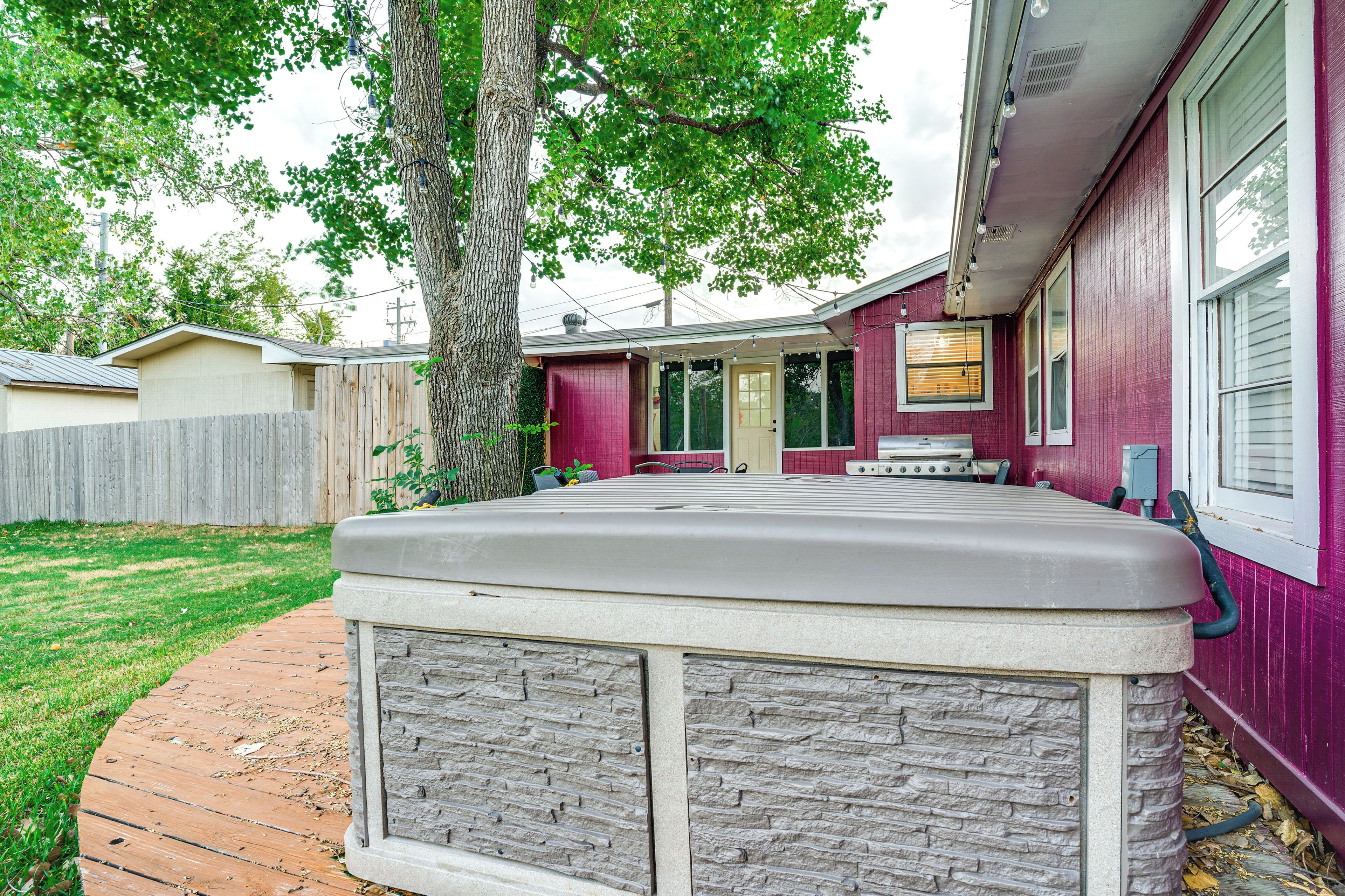 A backyard with a hot tub, a wooden deck, and a house with a red exterior.